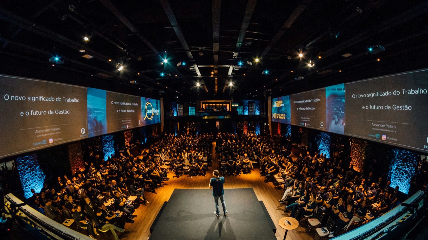 A speaker alone on a round stage, with a full auditorium seated around them in the dark.